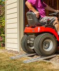 Person using Dual Runner Shed Ramps 3 Foot Long With Aluminum Serrated Rungs, Heavy Duty 1,500 Pound Capacity For Easy Loading Of Lawn Mowers, Snow Blowers, And Equipment Into Your Shed, Barn, Or Garage to load a lawn mower into a shed. The lawn mower is shown halfway up the aluminum ramp.