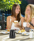 Two women enjoying coffee outdoors with Portable Turkish Coffee Pot 600ml Electric Kettle on table.