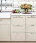 Cream kitchen cabinets with metal handles, fruits and flowers on countertop, modern faucet, brick backsplash, white sink