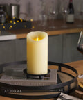 Ivory Flameless LED Pillar Candle With Moving Flame on a table in a cozy setting, 4 Inch by 7 Inch, real wax, scalloped edge.