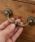 12 Pack Antique Bronze Drop Bail Pulls For Cabinets And Dressers, 3.5 Inch Center To Center, being attached to a wooden drawer.