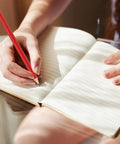 Person writing in notebook with a red pencil, emphasizing use for note taking and sketching, highlighting smooth writing quality.