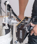 Person using a drywall box filler valve for joint compound pumps, heavy duty billet aluminum body with hard coat anodized finish, longer than standard length for easier no fuss filling, compatible with most pumps in action.