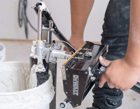 Person using a drywall box filler valve for joint compound pumps, heavy duty billet aluminum body with hard coat anodized finish, longer than standard length for easier no fuss filling, compatible with most pumps in action.
