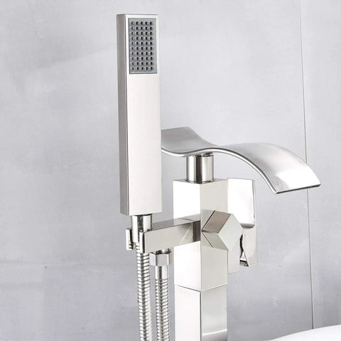 Close-up of floor mounted tub filler faucet with handheld sprayer and waterfall spout in brushed nickel finish.