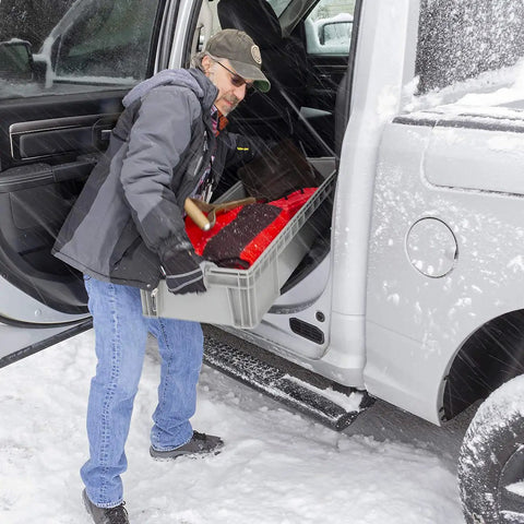 Person loading Heavy Duty Plastic Storage Tote With Straight Wall Design 48 Inch By 15 Inch By 7.5 Inch into vehicle in snow