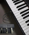 Three-Foot Pedal Unit For Digital Pianos And Keyboards With Universal 5-Pin Round Interface next to piano keys, metal pedals visible