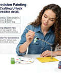Woman using Must-Have Helping Hands Soldering Tool With Steel Base And Adjustable Joint Clamp for painting, with supplies on table.