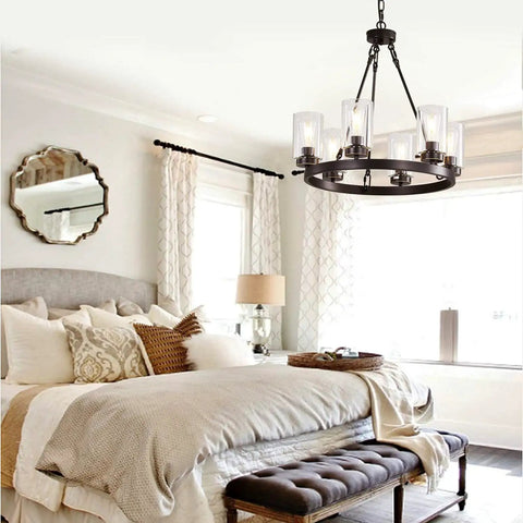 Six Light Industrial Rustic Farmhouse Wagon Wheel Chandelier In Black Metal With Clear Glass Shades above a bed.
