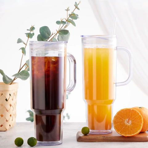 Two 40 Oz Clear Double Wall Acrylic Tumblers With Handle And Straw Lid, one with iced coffee, the other with juice.