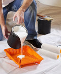 Person pouring white paint into an orange tray, featuring 10 Pack Mini Paint Roller Covers Plus Replacement Sleeves For Walls.