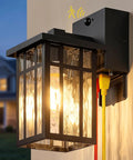 Heavy Duty Matte Black Motion Sensor Outdoor Wall Light With Built In GFCI Outlet mounted on a wall with illuminated glass shade.