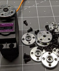 Six aluminum 25T servo horn discs with screws shown beside a black hobby servo