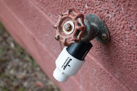 Low-Flow Drip Irrigation Pressure Regulator 25 PSI Three Quarter Inch Hose Thread attached to outdoor faucet on brick wall.