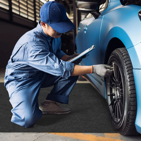 Mechanic inspecting tire over a 4 Pack 36 By 72 Inch Oil Spill Mat For Under Car And Garage Drips Absorbent Pads With Rubber Backing