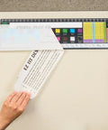 Applying EZ-Fit Desktop Helper Tape Strips Pack of 36 Student Desk Name Tags on classroom desk with colorful chart.