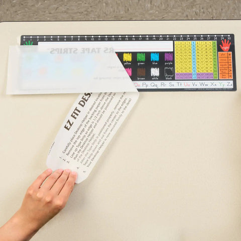 Applying EZ-Fit Desktop Helper Tape Strips Pack of 36 Student Desk Name Tags on classroom desk with colorful chart.