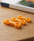 Set of three orange avian splay leg hobbles from 16 Piece Bird Splay Leg Treatment Ring Set With 3.5mm 4mm 5mm 6mm Holes on wood