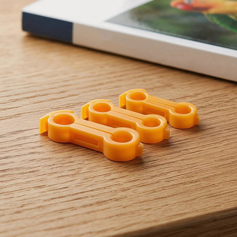 Set of three orange avian splay leg hobbles from 16 Piece Bird Splay Leg Treatment Ring Set With 3.5mm 4mm 5mm 6mm Holes on wood