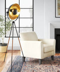 Lit Modern Tripod Floor Lamp in black with gold foil shade, leather legs, beside a beige armchair in living room.