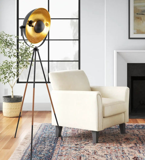 Lit Modern Tripod Floor Lamp in black with gold foil shade, leather legs, beside a beige armchair in living room.