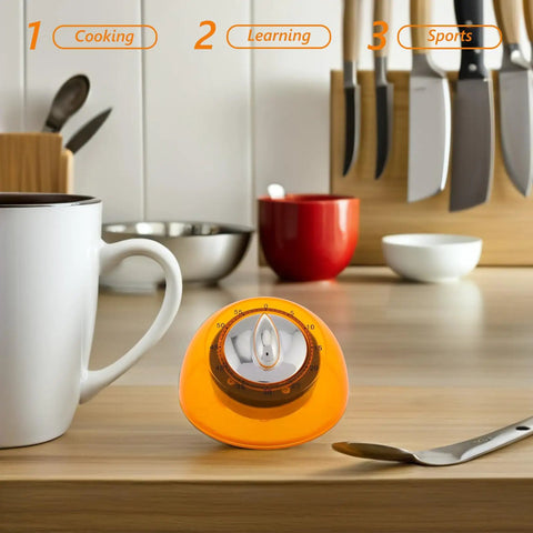 Orange Mechanical Kitchen Timer Wind Up Countdown Clock for Cooking and Baking, sits on a wooden counter with cups and utensils.