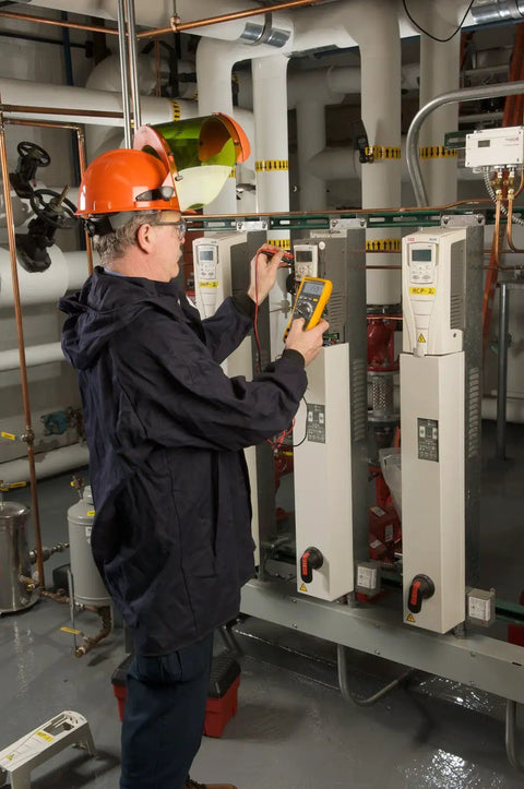 Technician using Pro Grade True RMS Digital Multimeter with Backlit Display and Built-In Temperature Probe in industrial setting.