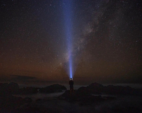 Person using Sentinel 2000 Lumen Rechargeable Flashlight with ultra-bright tactical beam at night under starry sky.