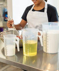 Woman using 64oz Half Gallon Measure Pitcher With Conversion Chart Heavy Duty Food Grade Polypropylene for cooking in kitchen.