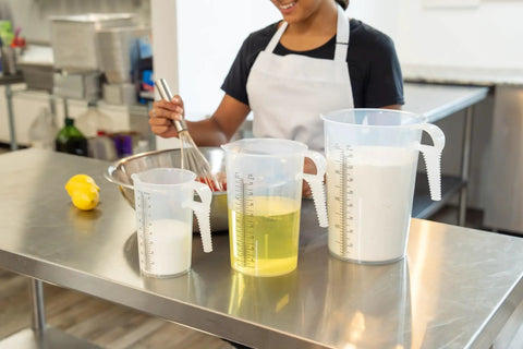 Woman using 64oz Half Gallon Measure Pitcher With Conversion Chart Heavy Duty Food Grade Polypropylene for cooking in kitchen.