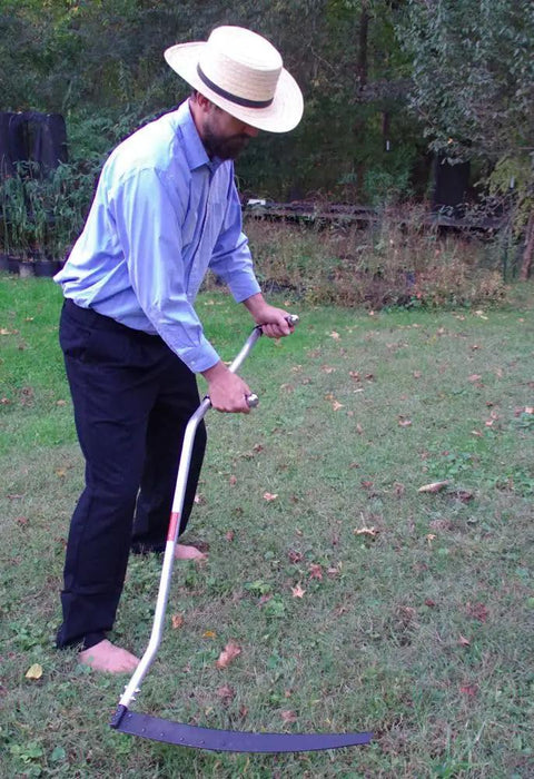 Man using Curved Metal Scythe Blade And Snath With A 53 Inch Handle 22 And A Half Inch Long Blade By 2 And A Quarter Inch Wide Reinforced Spine Made In USA Handcrafted For Light Brush Clearing Grass And Grain Work on grass field