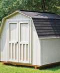A white outdoor shed with a shingled roof on a grassy area.