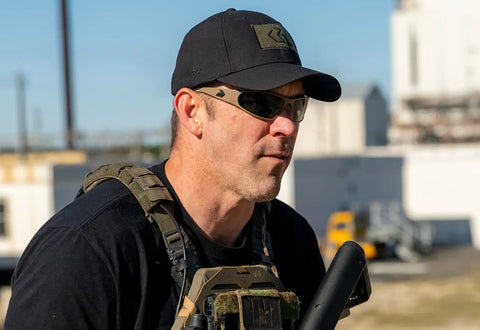 Heavy Hit Ballistic Safety Sunglasses Featuring Milspec Impact Resistant Wrap Frame And Ansi Certification worn by man in tactical gear outdoors.