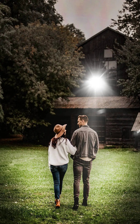 Couple walking under Hella Bright Outdoor LED Stadium Light 300W 42000 Lm 6500K IP67 illuminating a barn at night.
