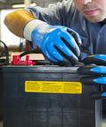 Worker wearing fully coated nitrile foam work gloves with nylon liner handling car batteries in a garage, 13 gauge large size.