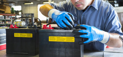 Worker wearing fully coated nitrile foam work gloves with nylon liner handling car batteries in a garage, 13 gauge large size.