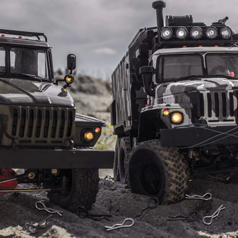 Two RC trucks on rocky terrain with silver and black RC body clips scattered around, showcasing Premium Universal RC Body Clips 120 Pieces Stainless Steel RC Clips Set For 1 To 10 And 1 To 12 Scale RC Cars Trucks Buggies Shell Replacement Silver And Black Durable Heavy Duty.