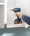 Bosch cordless impact driver (blue/black) driving a screw into white shelving.