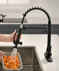 GIMILI Matte Black Commercial Kitchen Faucet with Pull Down Sprayer in use, rinsing oranges in a modern sink.