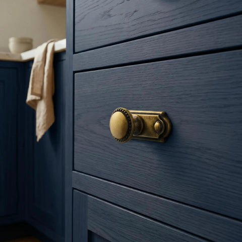 Close-up view of antique brass cabinet knob with industrial backplate on blue drawer, focusing on concealed design