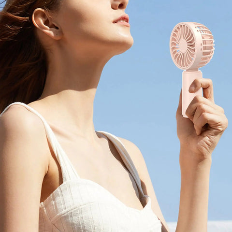 Person using a pink fan from the Four Pack USB Rechargeable Mini Handheld Fans Set With 3 Speeds against a blue sky.