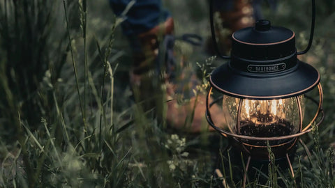 Antique Bronze LED Camping Lantern With Rechargeable Battery And USB Power Vintage Inspired Outdoor Light For Camping Backyard And Home Decor Adjustable Brightness Over 100 Hours On Low next to person in boots on grass.