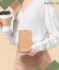 Person holding a coffee cup and a 2Lb Brown Paper Bags Pack Of 500 For Snacks Desserts And Small Dishes Takeout Durable 2 Pound Capacity Eco Friendly Recyclable Bag