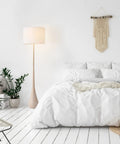 65 Inch Floor Lamp With Wood Toned Finish And White Cotton Shade Japandi Style E26 Base On Off Rotary Switch 5 Ft Cord Cozy Ambient Lighting Vibe For Living Room Or Bedroom next to a bed in a cozy bedroom setting.