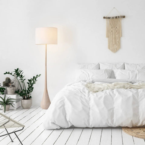 65 Inch Floor Lamp With Wood Toned Finish And White Cotton Shade Japandi Style E26 Base On Off Rotary Switch 5 Ft Cord Cozy Ambient Lighting Vibe For Living Room Or Bedroom next to a bed in a cozy bedroom setting.