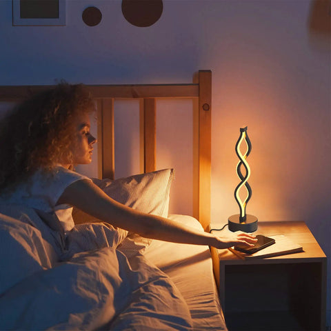 Woman reaching for Spiral LED Table Lamp With Dimmer In Slick Black Finish Touch Control Bedside Light With Three Color Temperatures 15.8 Inch Tall Modern Decor For Living Room And Bedroom on a nightstand.