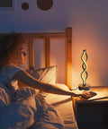 Set Of 2 Black Dimmable LED Bedside Lamps With Infinity Spiral Design next to a bed, lit in a cozy bedroom setting at night.