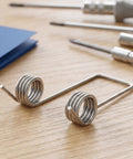 Heavy Duty Double Leg Torsion Springs For Trash Can Lid Repair Kit with 4 Coils Stainless Steel Garbage Bin Accessories Strong 130 Degree Angle Heavy Gauge Wire To Fix Stuck Lids Fast And Easy close-up on wood