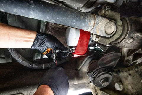 Heavy Duty Oil Filter Strap Wrench With Three Eighths And One Half Inch Drive Nylon Strap Forged Steel Handle Chrome Plated Drive in use under a truck