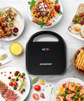 Aigostar 3 In 1 Electric Sandwich Maker With Removable Nonstick Plates on countertop surrounded by various delicious dishes.